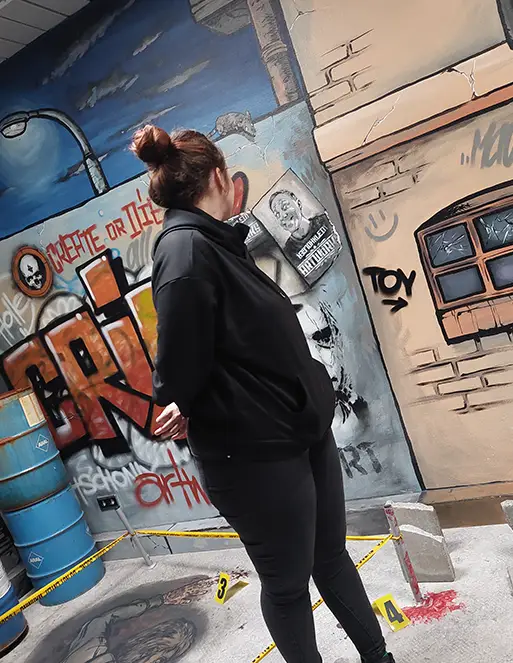 Eine Frau steht in einem Raum, der mit Graffiti besprüht ist. Sie dreht sich mit den Kopf nach hinten.