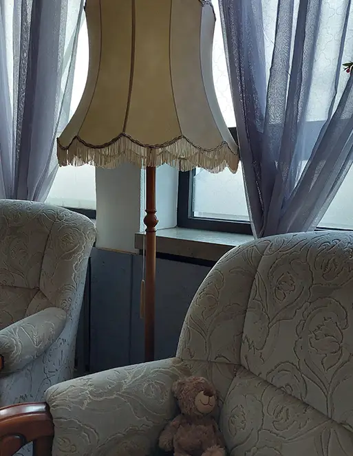 Auf dem Bild sind zwei Sessel. auf dem einem Sessel ist ein brauner Teddybär. Zwischen den Sesseln ist eine Stehlampe.